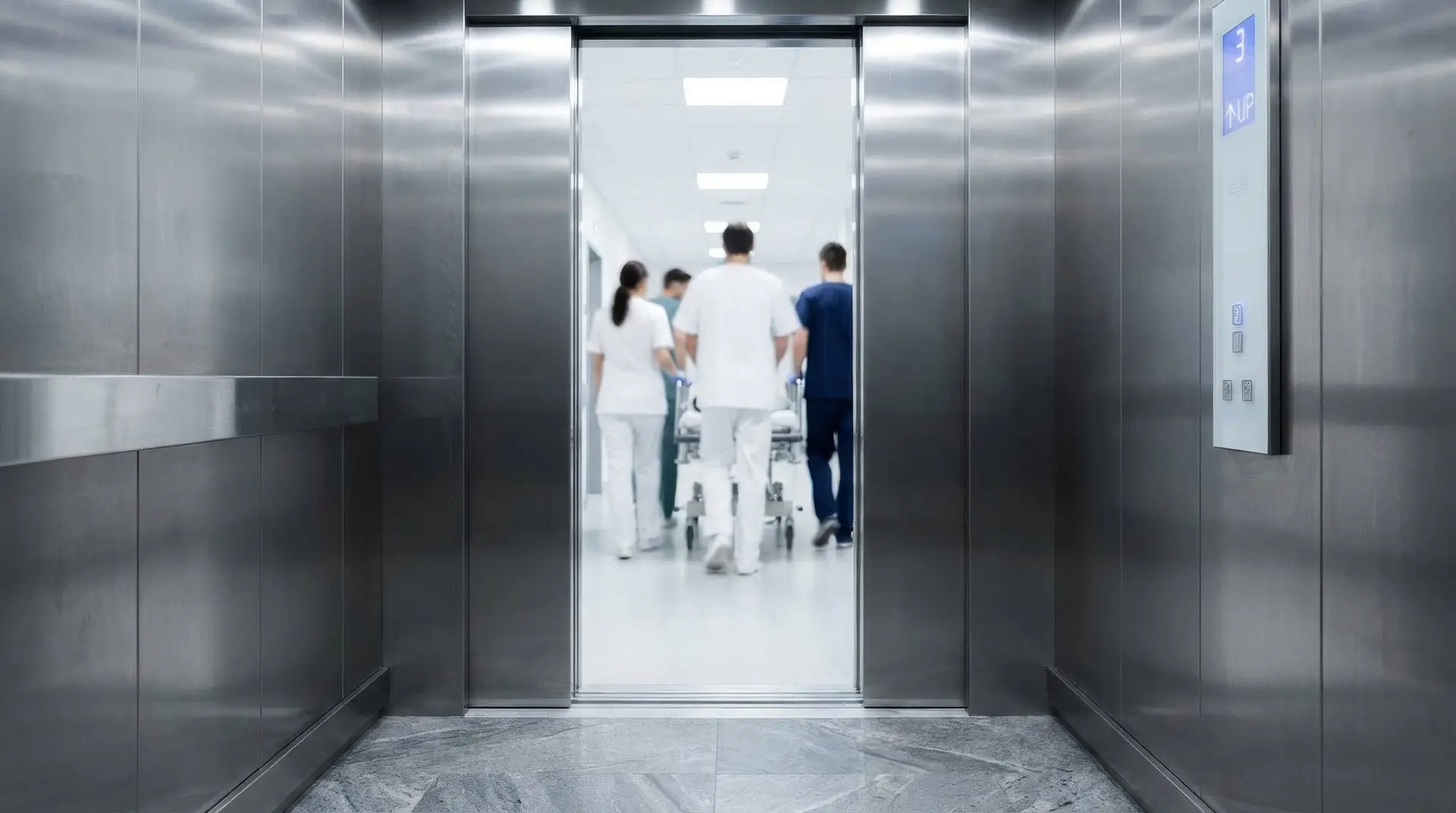 A group of people, some appearing to be medical staff, are seen from inside an elevator as they enter a bright, modern building interior.