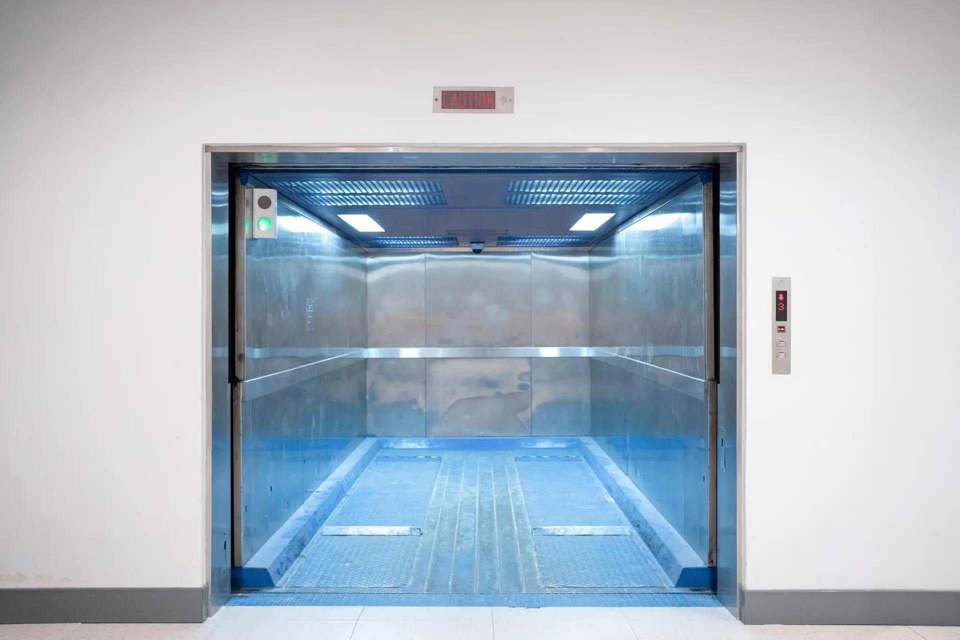 Modern freight elevator featuring a sleek two-section slide-up door design. Empty freight elevator